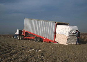 Image is an example of a cotton chain bed trailer with cotton modules being unloaded