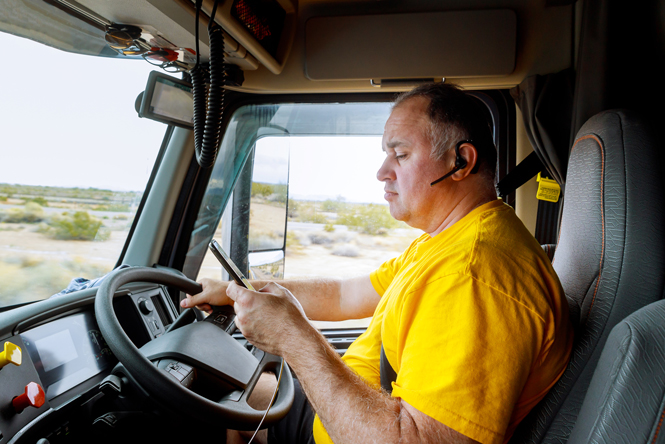 Image is of a man driving a truck but looking down at his mobile phone while driving.