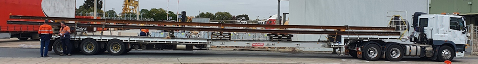 image is of a prime mover towing a semitrailer with a utility pole as it's load.